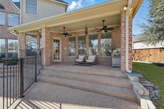 view of exterior entry with a ceiling fan, brick siding, and fence