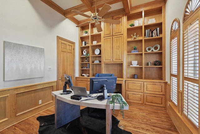 office featuring ceiling fan, a wainscoted wall, coffered ceiling, light wood-style floors, and beamed ceiling