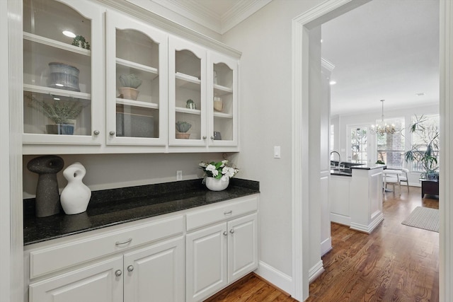 bar with crown molding, hanging light fixtures, dark wood-type flooring, a sink, and a chandelier