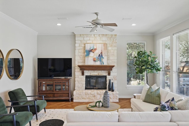 living area with ceiling fan, ornamental molding, wood finished floors, and a stone fireplace