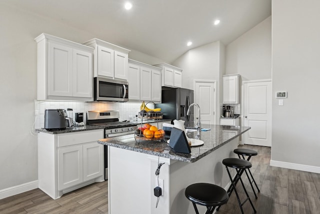 kitchen with light wood-type flooring, a kitchen breakfast bar, tasteful backsplash, white cabinetry, and appliances with stainless steel finishes