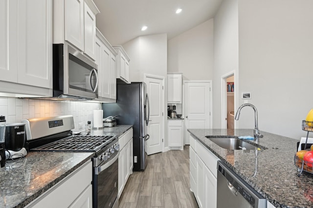 kitchen featuring a sink, dark stone countertops, backsplash, white cabinetry, and appliances with stainless steel finishes