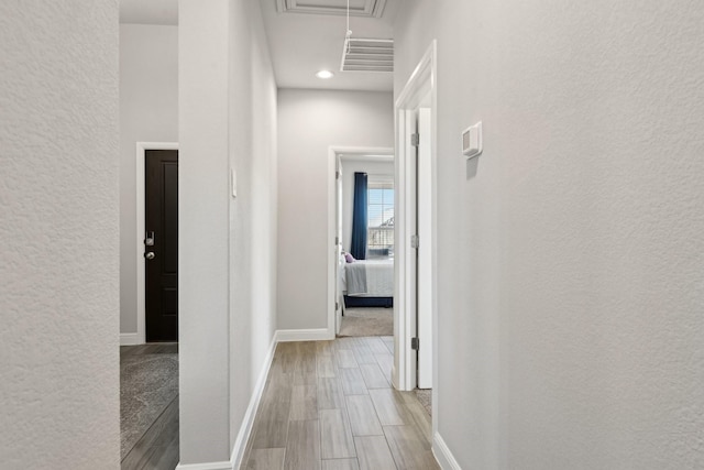 hall with wood finished floors, visible vents, baseboards, attic access, and a textured wall