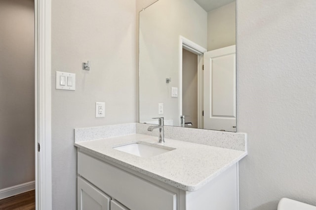 half bathroom with vanity, wood finished floors, and baseboards