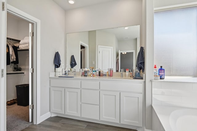 bathroom with wood finished floors, a bathing tub, double vanity, a sink, and a spacious closet