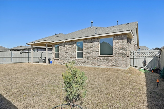 rear view of house with a yard, a fenced backyard, brick siding, and roof with shingles