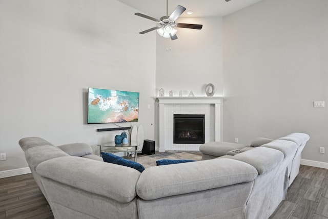 living room with baseboards, a fireplace, a towering ceiling, wood finished floors, and a ceiling fan