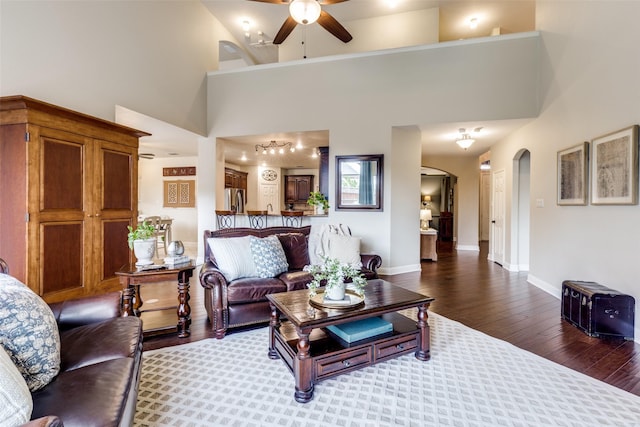 living room with arched walkways, wood finished floors, a towering ceiling, a ceiling fan, and baseboards