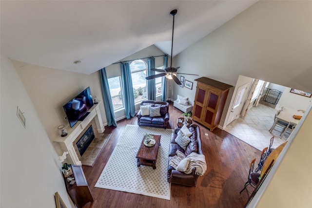 living room with high vaulted ceiling, wood finished floors, a glass covered fireplace, and a ceiling fan