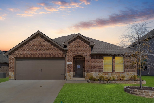 view of front of property featuring a garage, a shingled roof, brick siding, a yard, and stone siding