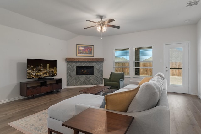 living area with plenty of natural light, a tiled fireplace, visible vents, and wood finished floors