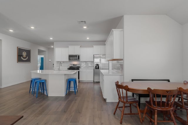 kitchen featuring visible vents, an island with sink, appliances with stainless steel finishes, a breakfast bar, and backsplash