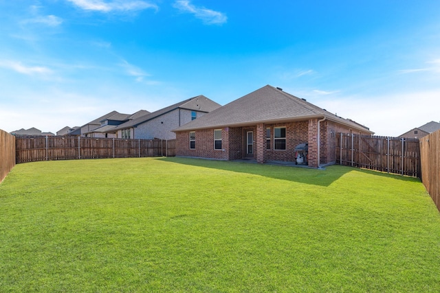 back of property featuring a yard, brick siding, a shingled roof, and a fenced backyard