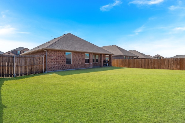 rear view of house with a fenced backyard, a shingled roof, a lawn, and brick siding