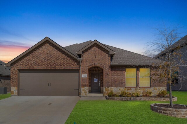 view of front facade with roof with shingles, a lawn, brick siding, concrete driveway, and stone siding