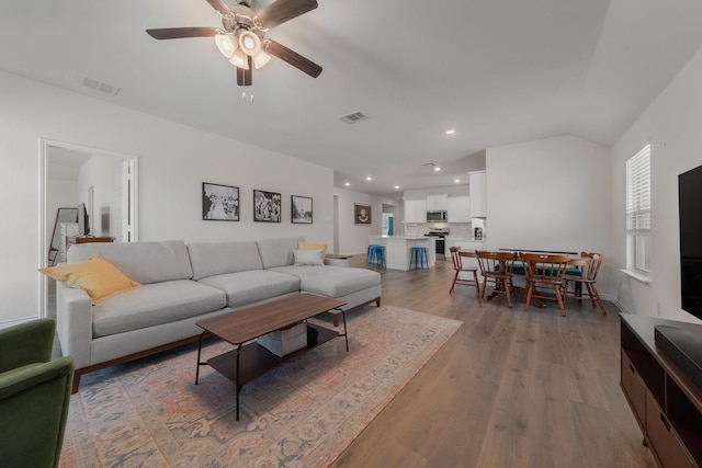 living room featuring ceiling fan, vaulted ceiling, visible vents, and light wood-style floors