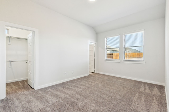 unfurnished bedroom featuring carpet, a walk in closet, vaulted ceiling, and baseboards