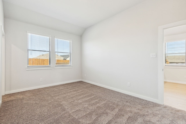 empty room with carpet floors, baseboards, and vaulted ceiling