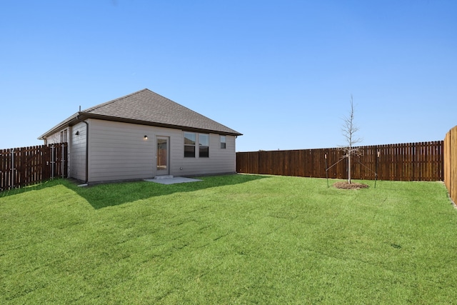 back of house featuring a shingled roof, a lawn, and a fenced backyard