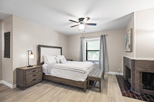 bedroom featuring light wood-type flooring, a brick fireplace, a ceiling fan, and baseboards