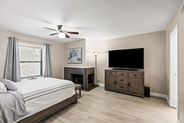 bedroom featuring ceiling fan, a fireplace, visible vents, baseboards, and light wood finished floors