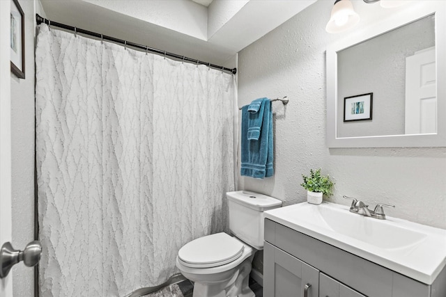 bathroom with a shower with shower curtain, a textured wall, vanity, and toilet