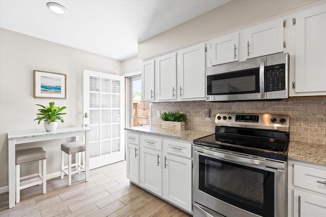 kitchen with light stone counters, light wood-style flooring, white cabinets, appliances with stainless steel finishes, and tasteful backsplash