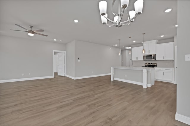 kitchen with stainless steel appliances, light wood-style flooring, open floor plan, white cabinets, and ceiling fan with notable chandelier