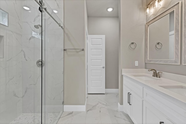 bathroom featuring marble finish floor, a marble finish shower, double vanity, a sink, and baseboards