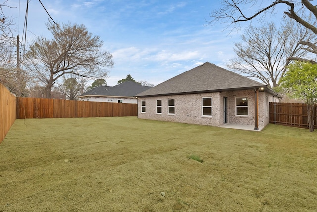 rear view of house featuring a fenced backyard, a shingled roof, a lawn, and brick siding