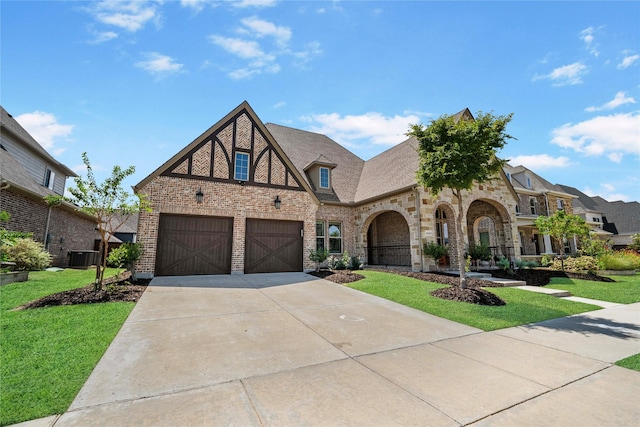 tudor-style house featuring a garage, brick siding, concrete driveway, and a front yard