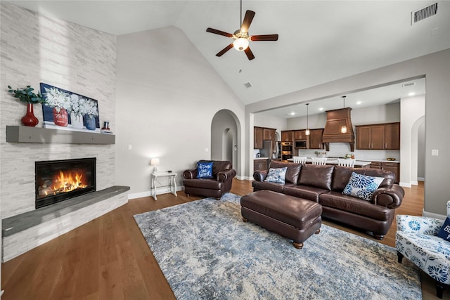 living area featuring arched walkways, high vaulted ceiling, a fireplace, and dark wood-style floors