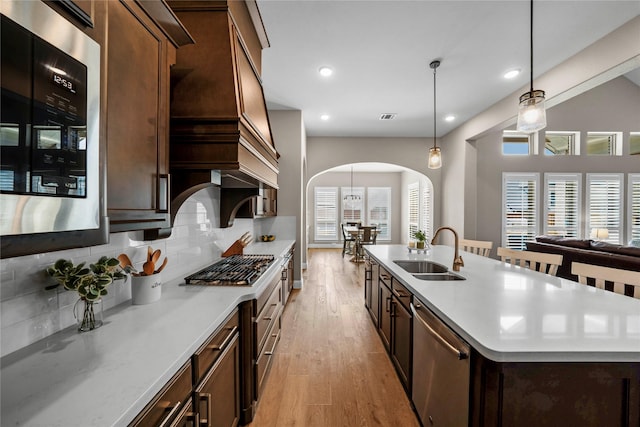 kitchen featuring a center island with sink, decorative backsplash, appliances with stainless steel finishes, a sink, and light wood-type flooring