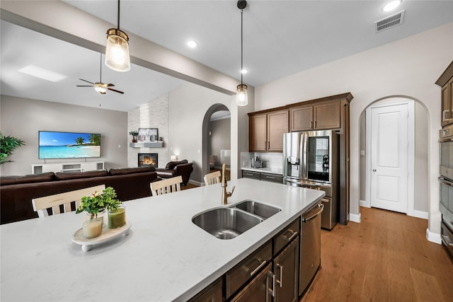 kitchen featuring a large fireplace, visible vents, arched walkways, appliances with stainless steel finishes, and a sink