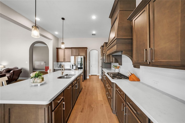 kitchen with arched walkways, light wood finished floors, stainless steel appliances, light countertops, and a sink