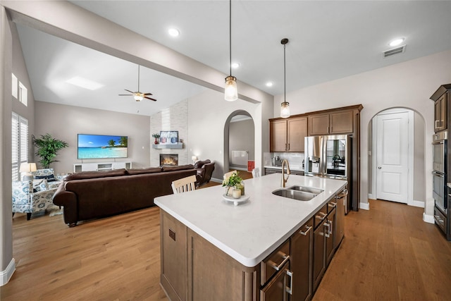 kitchen with a large fireplace, visible vents, arched walkways, stainless steel fridge with ice dispenser, and a sink