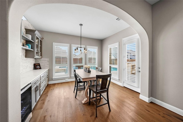 dining space featuring baseboards, arched walkways, wine cooler, light wood-type flooring, and a notable chandelier