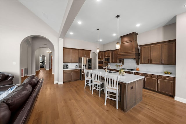 kitchen with a sink, a kitchen breakfast bar, open floor plan, appliances with stainless steel finishes, and custom range hood