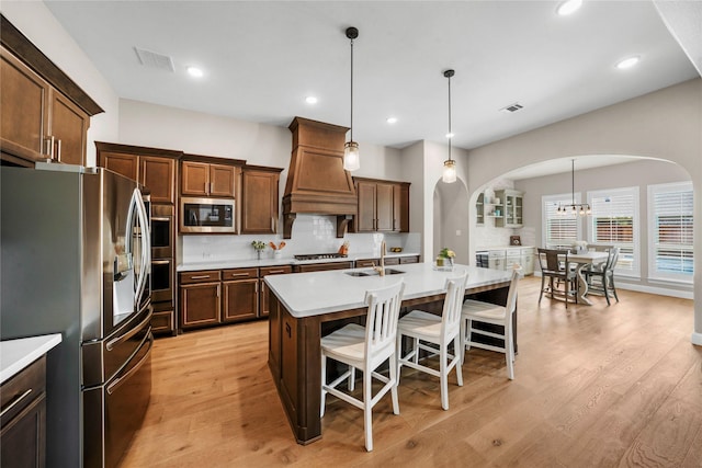 kitchen with arched walkways, light countertops, visible vents, appliances with stainless steel finishes, and premium range hood