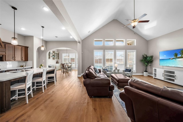 living area with high vaulted ceiling, arched walkways, light wood finished floors, and a ceiling fan