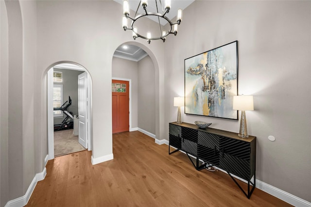 entrance foyer with arched walkways, light wood-style flooring, a towering ceiling, baseboards, and an inviting chandelier