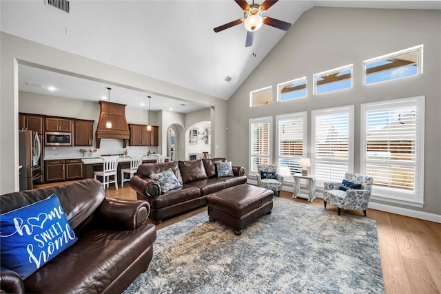 living room featuring arched walkways, visible vents, ceiling fan, wood finished floors, and high vaulted ceiling