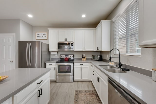 kitchen with white cabinets, stainless steel appliances, light countertops, a sink, and light wood-type flooring