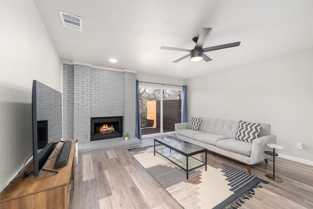 living area featuring visible vents, baseboards, a ceiling fan, wood finished floors, and a brick fireplace