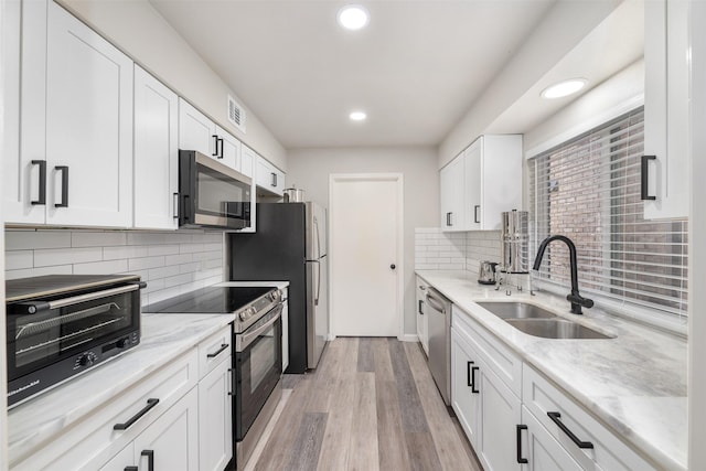 kitchen featuring a toaster, appliances with stainless steel finishes, white cabinets, a sink, and light wood-type flooring