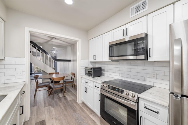 kitchen featuring stainless steel appliances, visible vents, white cabinetry, light stone countertops, and light wood-type flooring