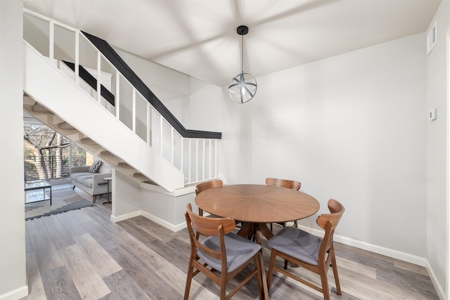 dining area with stairs, wood finished floors, visible vents, and baseboards