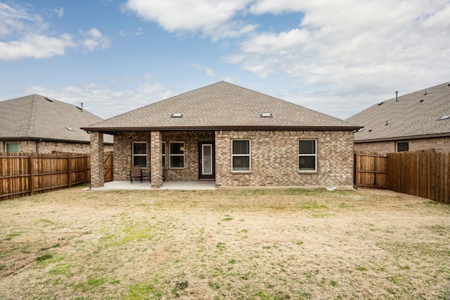 rear view of house featuring a patio, a fenced backyard, roof with shingles, a yard, and brick siding