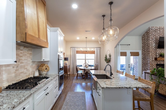 kitchen featuring dark wood-style floors, a center island with sink, tasteful backsplash, stainless steel gas stovetop, and a kitchen breakfast bar