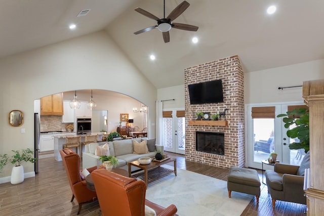 living room featuring arched walkways, a fireplace, light wood finished floors, visible vents, and high vaulted ceiling